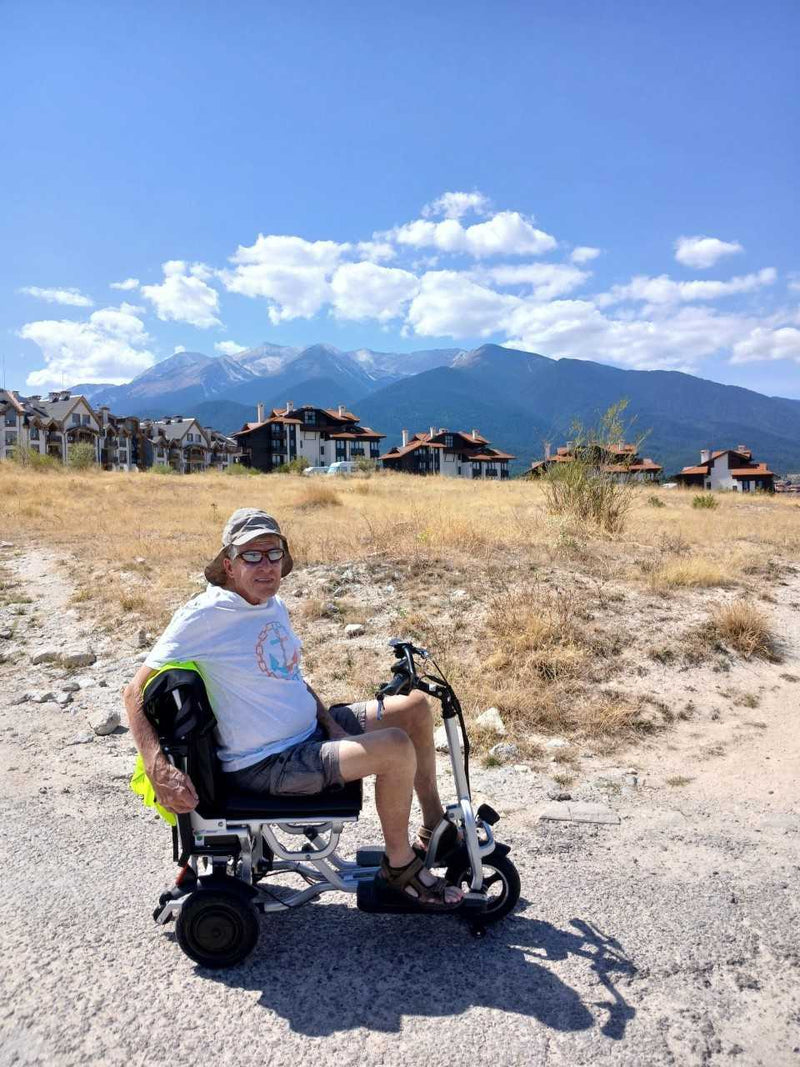 A customer riding the folding scooter on a gravel track with mountains behind