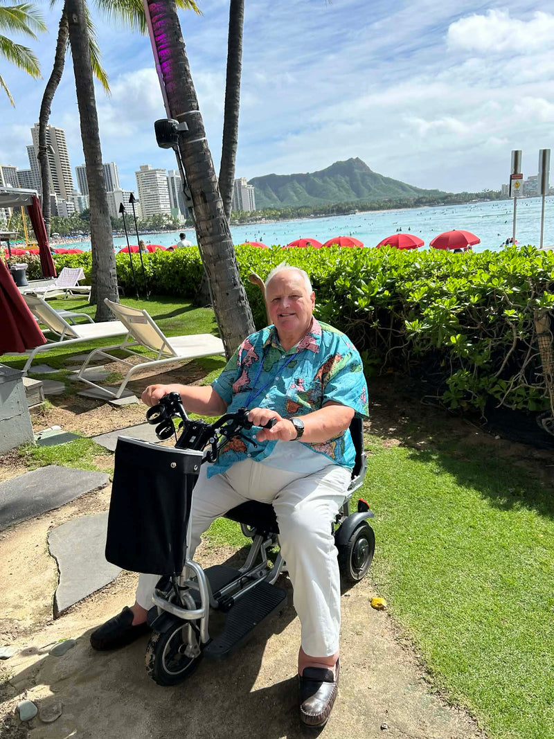 A customer on the folding scooter beside a palm-lined beach while on holiday
