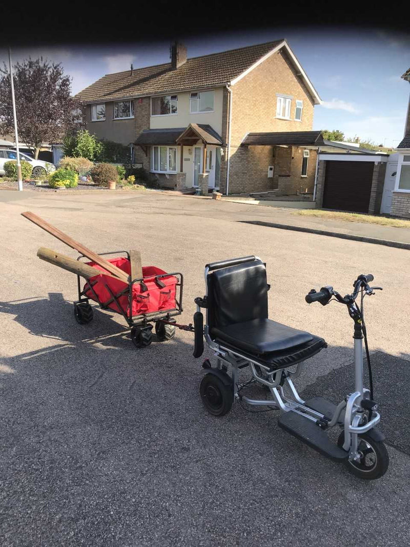 A customer's scooter on a driveway, parked beside a loaded garden trolley